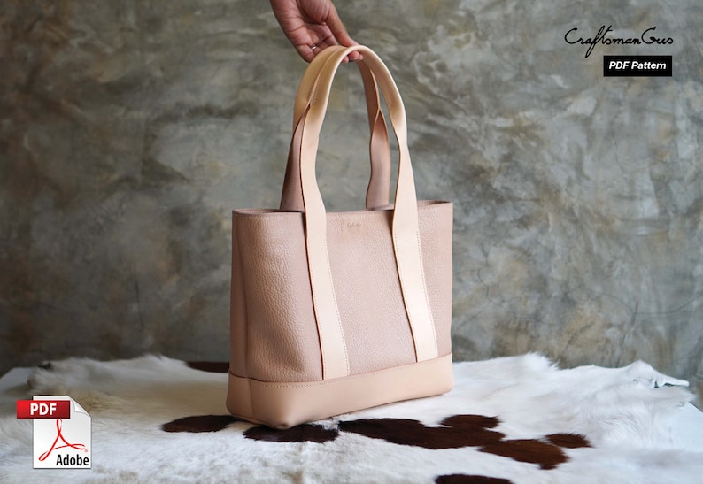 May include: A light pink leather tote bag with light beige straps and base. The bag has a rectangular shape and is held by a hand. The text "Craftsman Gus PDF Pattern" is visible in the upper right corner.
