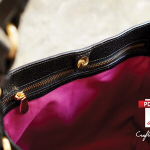 May include: The inside of a black leather handbag with a gold zipper and a pink lining. The zipper has a gold pull with a small decorative piece.