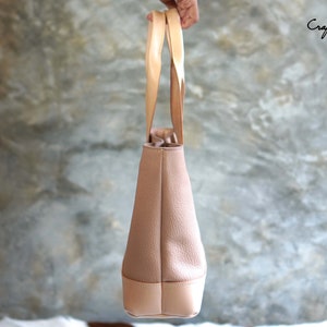 May include: A light brown tote bag with light tan handles and a light tan bottom. The bag has a textured surface and is held up by a person. The text "Craftsman Gus PDF Pattern" is in the upper right corner.