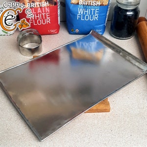 May include: A silver baking tray with slightly curved edges. The baking tray is sitting on a wooden chopping board.