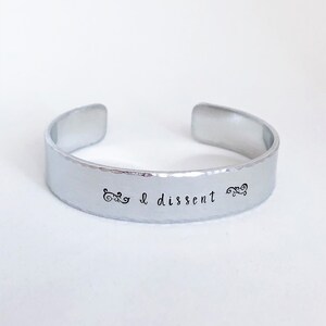 May include: A silver metal bracelet with the words "I dissent" engraved on it.