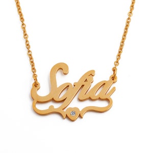 May include: Gold-colored necklace with the name "Sofia" in a cursive font. A small heart with a single clear gemstone is below the name. The necklace chain is also gold-colored.