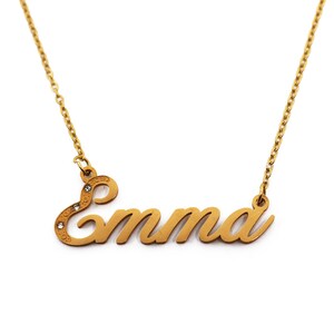 May include: A gold-colored necklace with the name "Emma" in a cursive font. The pendant has small, clear gemstones and hangs from a delicate chain. The necklace is displayed against a white background.