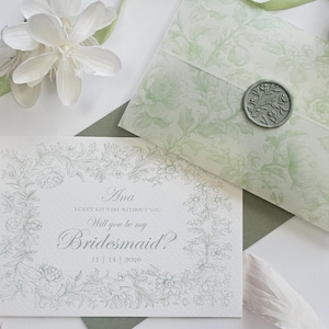 May include: A white bridesmaid proposal card with grey floral borders and text reading Ana, I can't say I do without you, Will you be my Bridesmaid?, 11 | 14 | 2026. It includes a sage green floral envelope with a wax seal and silk ribbons.