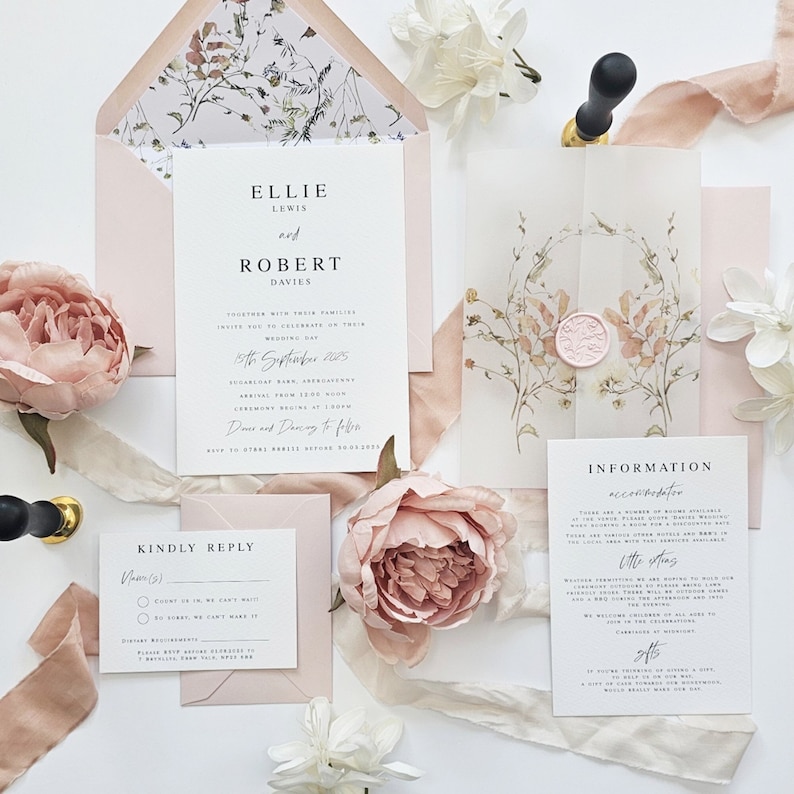 Op de afbeelding: Een huwelijksuitnodigingsset met een bloemenontwerp. De uitnodiging is gedrukt op wit karton met een roze envelop. De RSVP-kaart is gedrukt op wit karton met een roze envelop. De informatiekaart is gedrukt op wit karton met een roze envelop. De tekst op de uitnodiging luidt "Ellie Lewis en Robert Davies, 15 september 2025, De ceremonie begint om 13:00 uur, Dansen en dansen daarna".