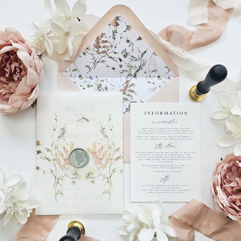 Op de afbeelding: Een huwelijksuitnodigingsset met een bloemenontwerp. De uitnodiging is wit met een aquarelbloemenkrans en een waszegel. De informatiekaart is wit met zwarte tekst en bevat details over de bruiloft, zoals de datum, tijd en locatie. De envelop is roze met een bloemenpatroon.