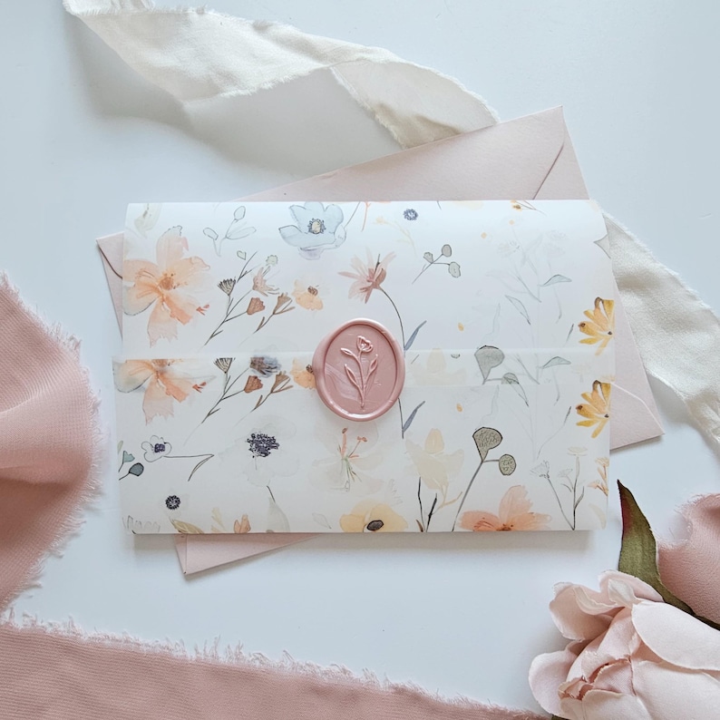 May include: A floral-patterned invitation suite featuring a white envelope with watercolor flowers in peach, yellow, and blue. A pink wax seal with a floral design secures the invitation. Soft pink ribbons and a matching envelope complete the elegant design.