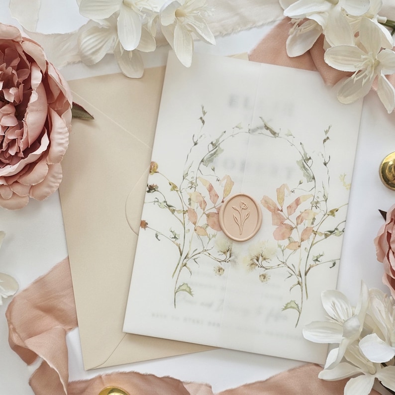 Op de afbeelding: Een witte huwelijksuitnodiging met een bloemenontwerp en een perzikkleurige waszegel. De uitnodiging zit in een beige envelop met een perzikkleurig lint.