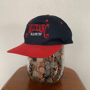 May include: A navy blue and red baseball cap with the embroidered text "Mustang Ranch" in red.