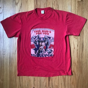 Könnte beinhalten: Rotes T-Shirt mit einer Vintage-Budweiser-Werbung mit Onkel Sam und dem Text "This Bud's For You".