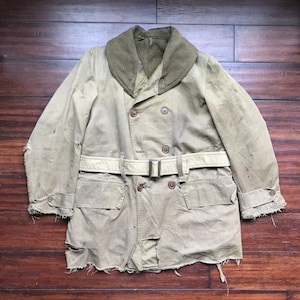 May include: A vintage, double-breasted, tan canvas coat with a green corduroy collar and a belt. The coat has a frayed hem and cuffs, and is in worn condition.