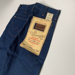 May include: A pair of blue denim jeans with a brown paper tag that reads "Wrangler Student Cowboy Cut 100% Cotton 14 1/2 Ounce Pre-Shrunk Made in U.S.A. One Year Warranty".