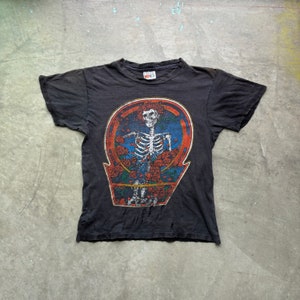 May include: Black t-shirt with a vintage Grateful Dead "Steal Your Face" graphic featuring a skeleton in a circle of red roses.