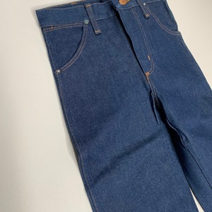 May include: A pair of dark blue denim jeans with a classic five-pocket style. The jeans have a straight leg and a button fly.