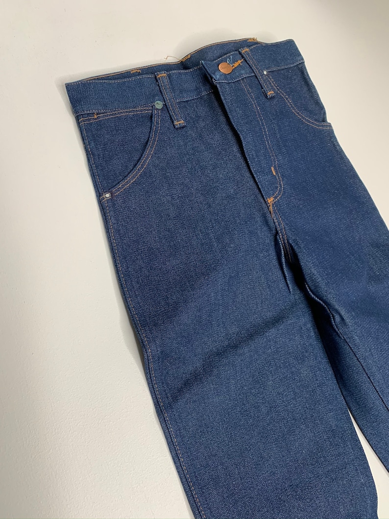 May include: A pair of dark blue denim jeans with a classic five-pocket style. The jeans have a straight leg and a button fly.