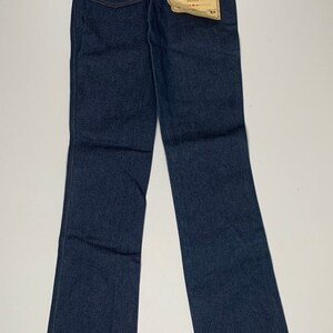 May include: A pair of dark blue denim jeans with a bootcut style. The jeans have a label on the back pocket that reads "Wrangler Student Cowboy Cut Pre-Shrunk".