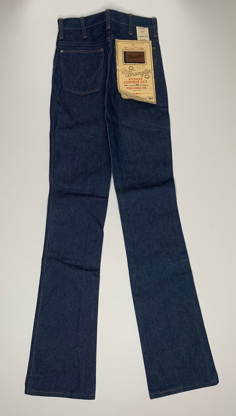 May include: A pair of dark blue denim jeans with a bootcut style. The jeans have a label on the back pocket that reads "Wrangler Student Cowboy Cut Pre-Shrunk".