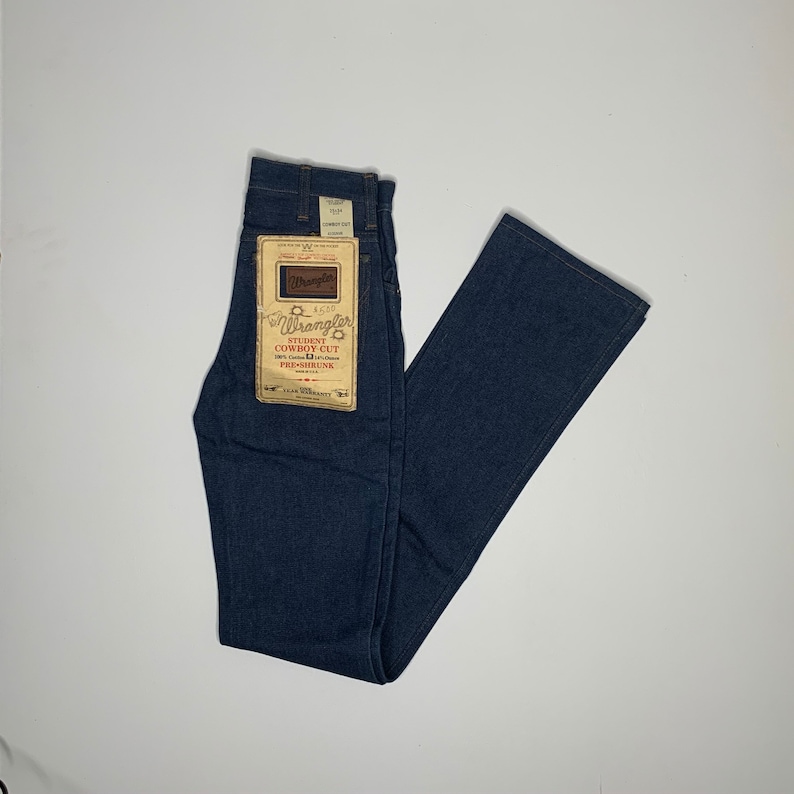 May include: A pair of dark blue denim jeans with a label that reads "Wrangler Student Cowboy Cut 100% Cotton Preshrunk" and a 1-year warranty.
