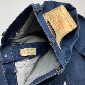 May include: A pair of blue denim jeans with a Wrangler label and a vintage "Cowboys Blue" label. The jeans are turned inside out to show the stitching and the label.