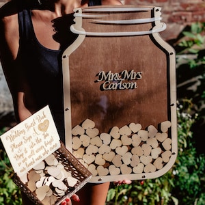 May include: Wooden wedding guest book alternative with a mason jar design. The jar is filled with wooden hearts and has a sign that says "Mr. & Mrs. Carlson".