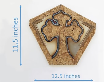 May include: A decorative wall art piece featuring a metal cross design set within a geometric frame. The cross is made of dark metal with blue accents, mounted on a wood composite background. The piece measures 11.5 inches high and 12.5 inches wide.