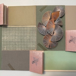 May include: A collage of book covers and paper fans in shades of green, brown, and pink. The book covers feature a repeating pattern of small crosses and a floral design. The paper fans are arranged in a cluster and are made of folded paper.