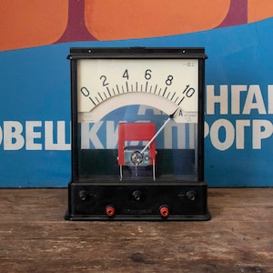 Puede incluir: Un amperímetro analógico negro con una cara blanca y una aguja roja. El amperímetro tiene una escala de 0 a 10 amperios y está etiquetado como "0.1". El amperímetro está montado en una base de metal negro con tres terminales.