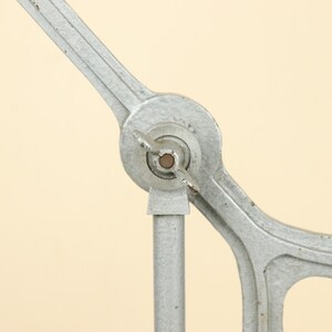 May include: A close-up of a silver metal machine with a round knob and a long arm. The machine has a vintage look and is made of metal.