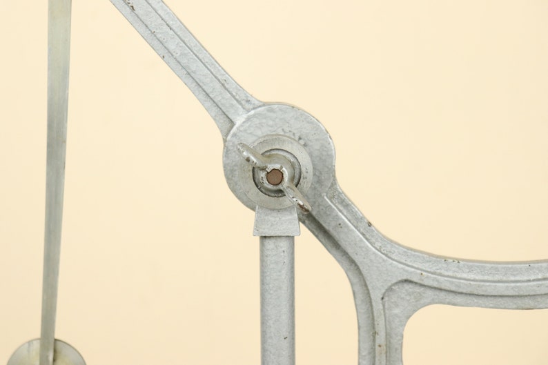 May include: A close-up of a silver metal machine with a round knob and a long arm. The machine has a vintage look and is made of metal.
