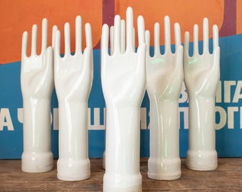 May include: Set of seven white ceramic mannequin hands with outstretched fingers. The hands are all identical and are arranged in a row on a wooden surface.