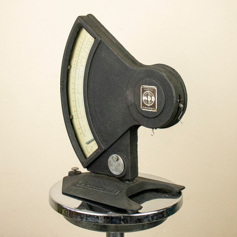 May include: A black vintage scale with a round dial and a metal base. The scale has a white face with black markings and the text "M. DEPRASSE" on the base.