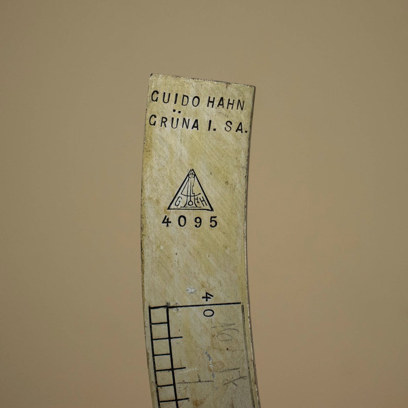 May include: Close-up of a white measuring tool with black markings. The tool is labeled "GUIDO HAHN GR&Uuml;NA I. SA." and has a triangular logo with the letters "G.H." inside. The number "4095" is printed below the logo.