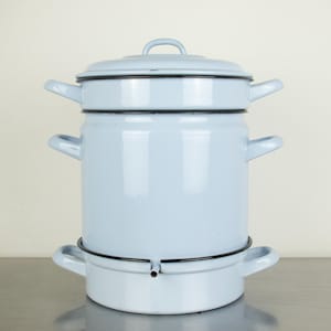 Op de afbeelding: Een lichtblauwe emaille koffiepot met een deksel en meerdere secties. De pot heeft een zwarte rand en handvatten. Een vintage keukenartikel.