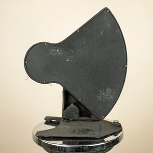 May include: A black metal vintage scoreboard with a large, round, blank display area. The scoreboard is mounted on a chrome base.