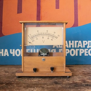 Può includere: Un voltmetro analogico vintage in legno con un quadrante in vetro trasparente e un ago nero. Il quadrante è contrassegnato da numeri da 0 a 25 e dalla lettera "V".