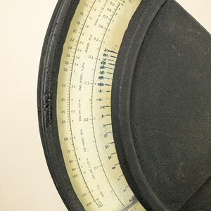 May include: A black circular scale with a white face and a needle. The scale is marked with numbers from 10 to 200 and has labels for grams, deniers, and meters. The scale is used to measure the weight and thickness of yarn.