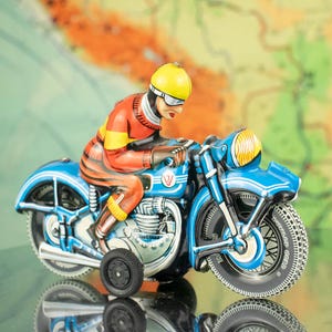 Może przedstawiać: Zabawkowy motocykl w kolorze niebieskim i czerwonym z kierowcą w żółtym kasku. Motocykl ma czarną i białą oponę z nadrukiem "Champion Gear".