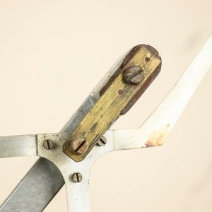May include: Close-up of a vintage drafting tool with a brass and wood adjustable arm. The tool has a silver metal base and several screws.