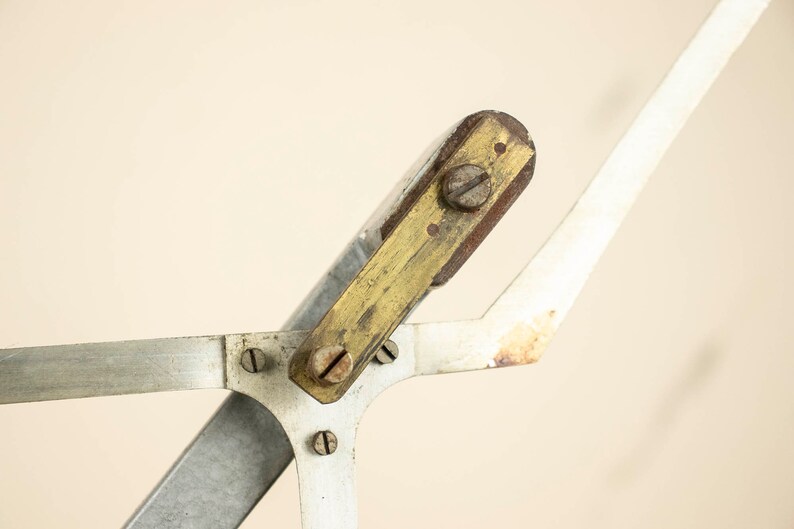 May include: Close-up of a vintage drafting tool with a brass and wood adjustable arm. The tool has a silver metal base and several screws.