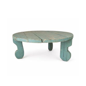 May include: A small, round, antique wooden table painted in a distressed light blue. The tabletop is made of several planks. The legs have a unique, curved design. The table is a charming piece of rustic furniture.