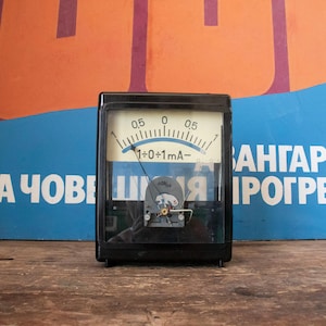 Peut inclure: Un compteur analogique noir avec un cadran blanc et une aiguille pointant vers 0. Le compteur a un boîtier en plastique noir et un cadran en verre. Le compteur indique "1+0+1mA-".