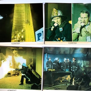 May include: Four lobby cards from the 1974 film "The Towering Inferno". The first card shows a helicopter flying over a burning skyscraper. The second card shows a fireman on the phone. The third card shows a fireman using a hose to fight a fire. The fourth card shows a group of firemen standing in a burning room.