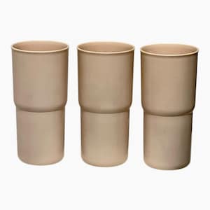 May include: Three beige, cylindrical tumblers. Each tumbler is composed of two stacked sections, creating a stepped design. The tumblers have a smooth, matte finish and a simple, modern aesthetic. The neutral color makes them versatile for various settings.