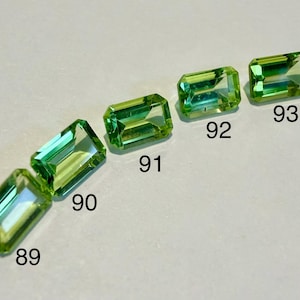 Peut inclure: Cinq pierres précieuses rectangulaires et facettées dans des tons de vert et de jaune sont disposées en diagonale. Chaque gemme est numérotée, avec les chiffres 89, 90, 91, 92 et 93 visibles. Les gemmes ont une surface polie et réfléchissante.