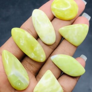 May include: A collection of seven green and white cabochon gemstones. The gemstones are various shapes, including oval, teardrop, and triangular.