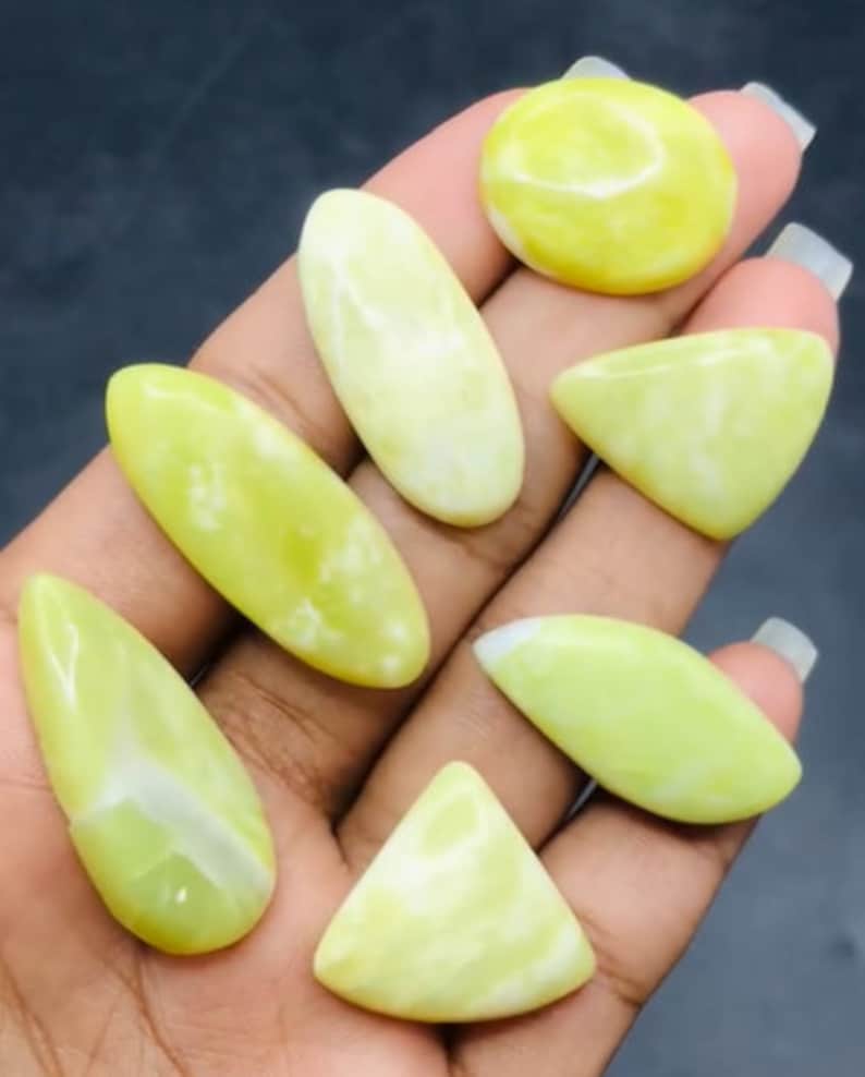May include: A collection of seven green and white cabochon gemstones. The gemstones are various shapes, including oval, teardrop, and triangular.