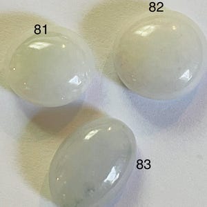 May include: Three smooth, white, oval-shaped stones with the numbers 81, 82, and 83 printed on them.