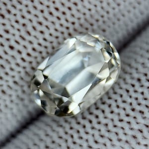 May include: A clear, faceted, oval-shaped gemstone with a slightly cloudy appearance.