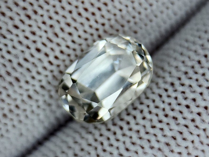 May include: A clear, faceted, oval-shaped gemstone with a slightly cloudy appearance.