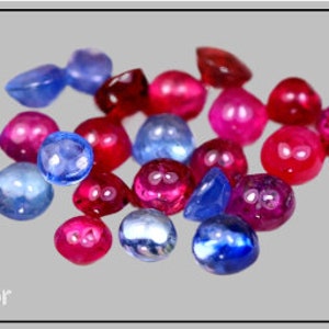 Puede incluir: Una colección de gemas pulidas en varios tonos de azul y rojo. Las gemas son de forma redonda y ovalada, con una superficie brillante. La imagen está tomada sobre un fondo gris, resaltando los colores y texturas de las piedras.